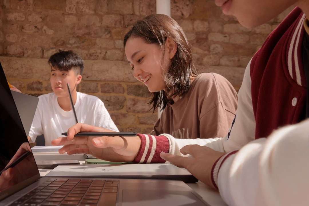 Three students working on laptops and in notebooks