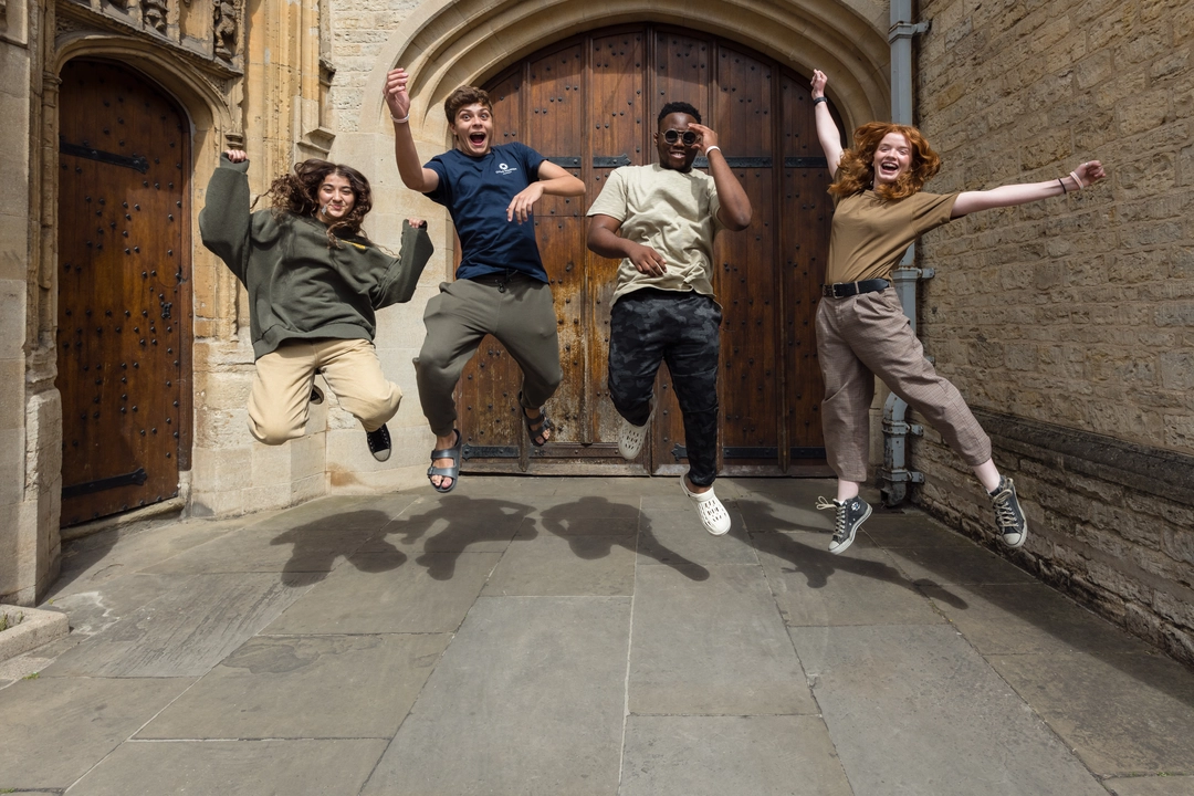 Four students jumping in the air, outside of an Oxford college building