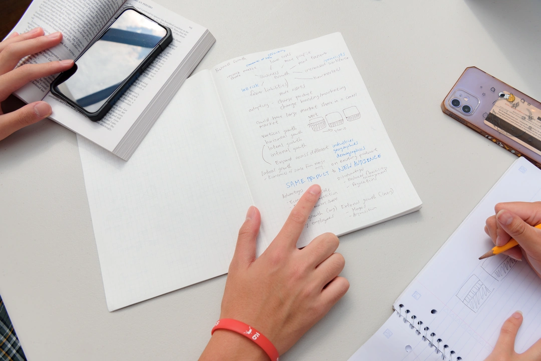 Close up of a student's notebook, phone and textbook on a desk