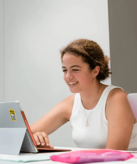 girl in a white top sat smiling in from of her tablet